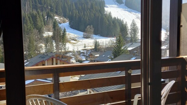 A balcony with wooden railings overlooking a snowy mountain landscape with houses and trees.