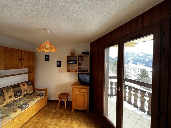 A cozy room with a wooden sofa, a small stool, a television, and a window with a snowy mountain view.