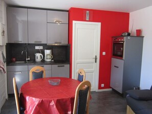 Una cocina compacta con una pared roja, una puerta blanca y una mesa de comedor con sillas.