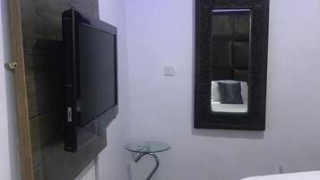 Ein kleines Hotelzimmer mit einem Bett, einem an der Wand befestigten Fernseher, einem kleinen Tisch und einem Spiegel.