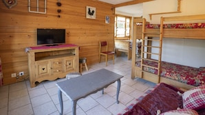Et hyggeligt værelse med trævægge, køjeseng, skrivebord med stol, fjernsyn og et lille bord.