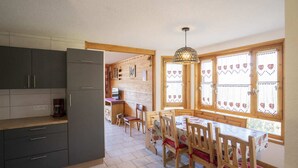 Et køkken med grå skabe, et spisebord med træstole og et vindue med hjerte-mønstrede gardiner.
