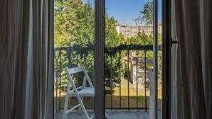 A room with a large sliding glass door leading to an outdoor balcony with a metal railing and a white chair.