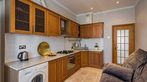 A compact kitchen with wooden cabinets, a built-in oven, a washing machine, and a dining area with a sofa.