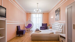 A bedroom with a bed, two chairs, a hanging chair, a TV, and a painting on the wall.