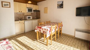 Een kleine keuken met houten kastjes, een magnetron, een spoelbak en een eettafel met stoelen.