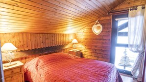 A cozy room with a wooden ceiling, a bed with a red quilt, two bedside tables with lamps, and a window with curtains. - 3-room apartment for 7 ppl, Châtel, pets allowed (Châtel)