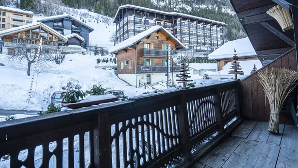 A wooden chalet with a balcony, surrounded by snow-covered buildings and a forested mountain backdrop. - 3-room apartment for 7 ppl, Châtel, pets allowed (Châtel)