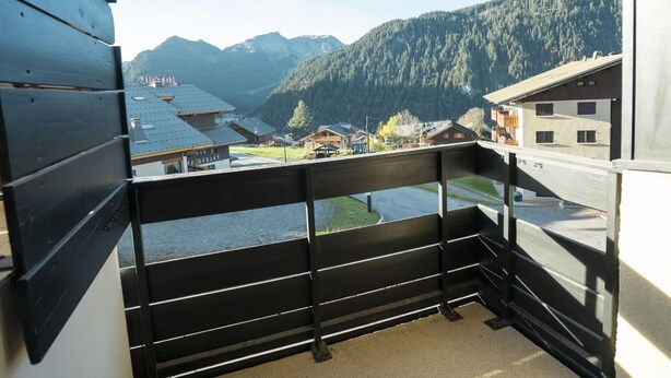Un balcon offrant une vue sur un village de montagne, des bâtiments en bois et un ciel dégagé.