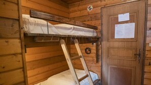 Une pièce de cabane en bois avec un lit superposé, une échelle et une porte sur laquelle est affiché un avis.