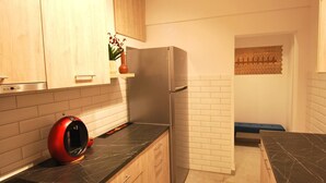 Une cuisine avec des meubles de couleur bois clair, un plan de travail en marbre noir, un réfrigérateur en acier inoxydable et un appareil de couleur rouge posé sur le plan de travail.