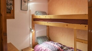 Een slaapkamer met een stapelbed met houten frame, een klein nachtkastje en een lijst met een afbeelding aan de muur.