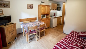 Een compacte kamer met een houten eettafel, een enkel bed, een kitchenette en een televisie.