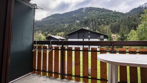 Een balkon met een houten hekwerk, een ronde tafel en een uitzicht op een berg en huizen op de achtergrond.