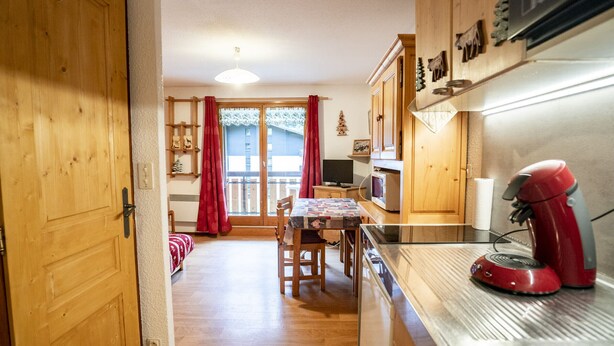 Een keuken met houten kastjes, een rode mixer en een eethoek met een tafel en stoelen.