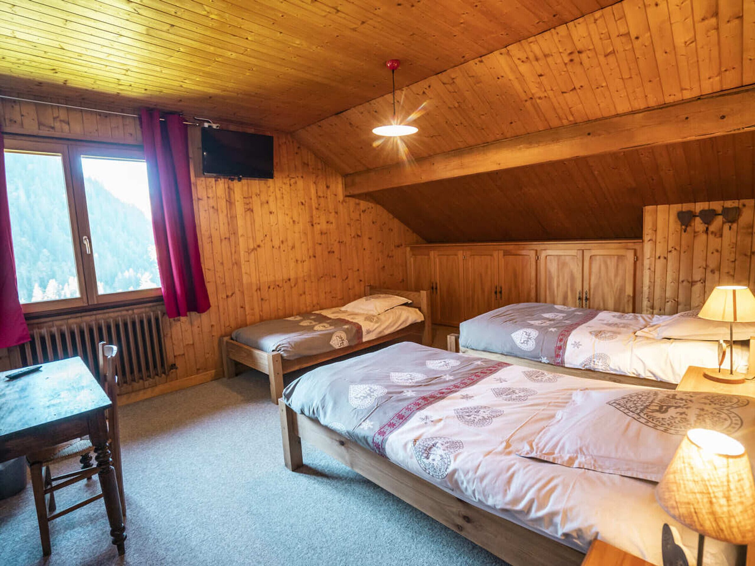 Ein gemütlicher Holzraum mit zwei Betten, einem Tisch und einem Fernseher.