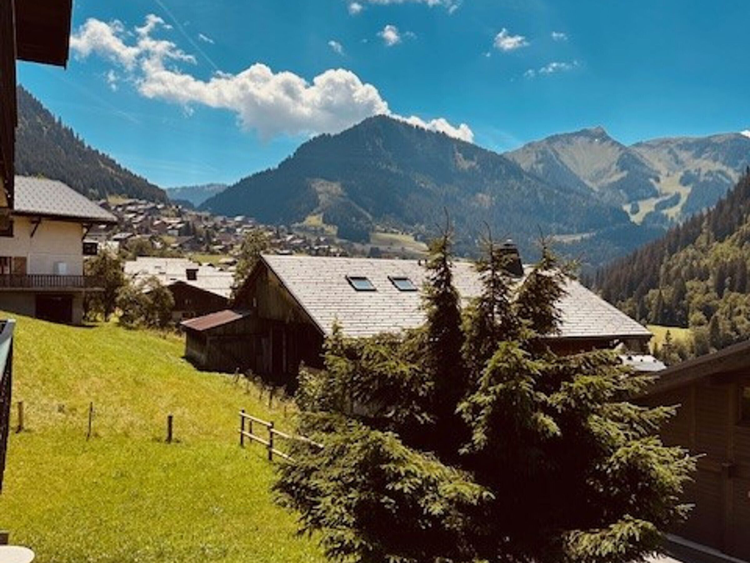 Een landelijk bergdorpslandschap met traditionele huizen, een grasheuvel en een vallei met bergen op de achtergrond.