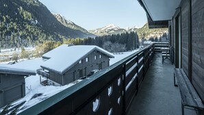 A wooden balcony with a view of snow-covered mountains and a building with a sloped roof. - Chalet in Châtel 6 bedrooms, 12 people (Châtel)