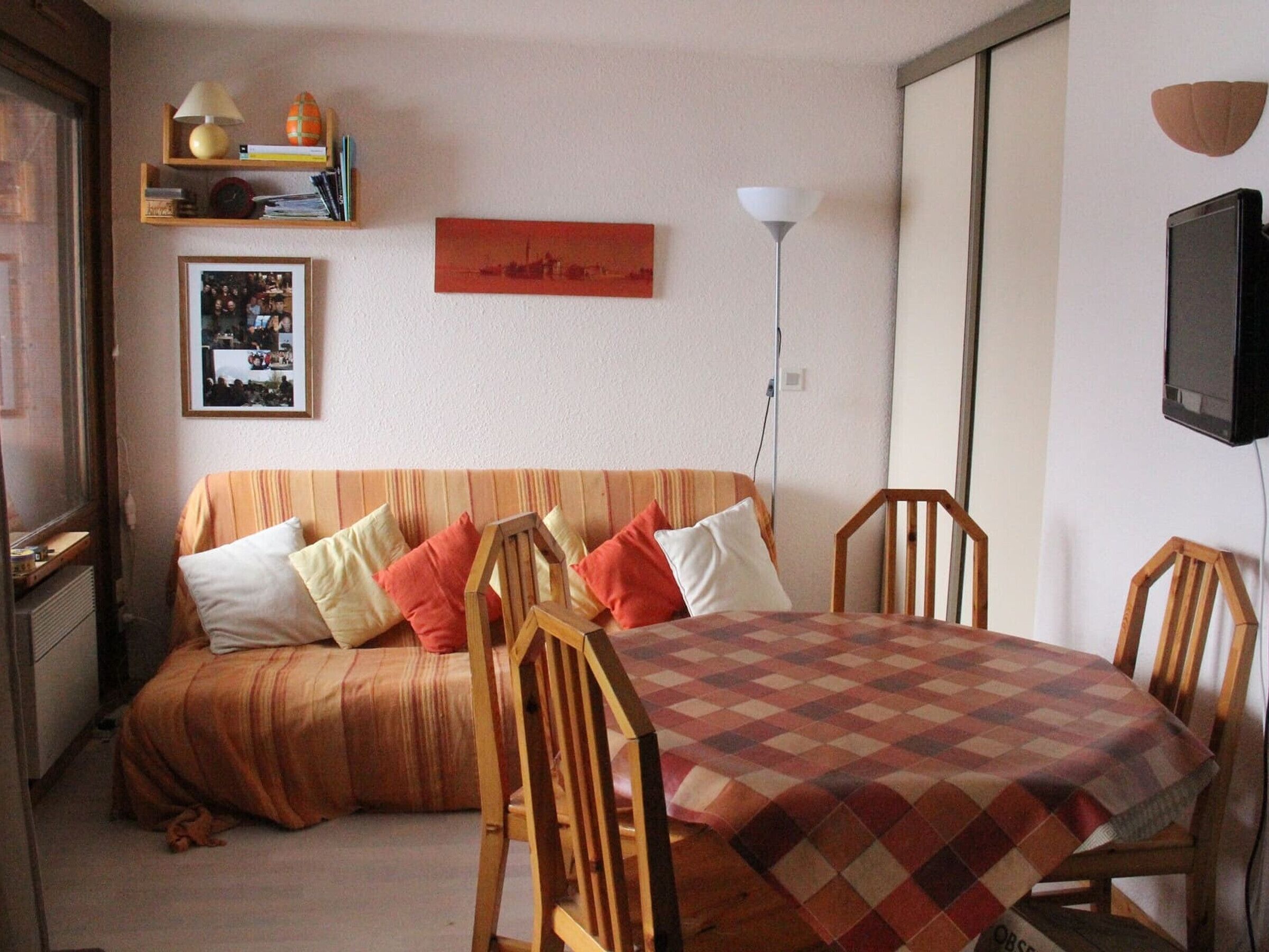 Een gezellige kamer met een bank, een eettafel met stoelen, een televisie en een lamp.
