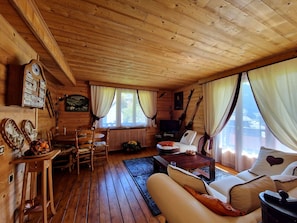 LâintĂ©rieur dâun chalet en bois, avec un canapĂ©, une table Ă manger, des chaises, un tĂ©lĂ©viseur et une cheminĂ©e.