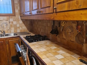 A kitchen with wooden cabinets, a gas stove, a sink, and hanging utensils.