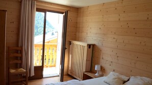 Une pièce en bois avec un lit, une chaise, un radiateur et une vue sur un balcon.