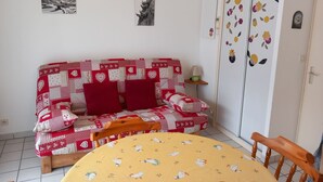 A cozy room with a red and white quilted sofa, a yellow tablecloth with duck patterns, and a wooden chair. - Studio Cozy in Châtel with Mountain View, Balcony, and Parking (Châtel)