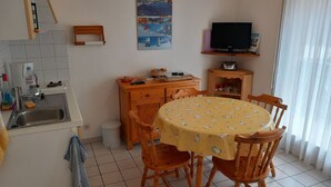 A compact kitchen with a sink, wooden cabinets, a dining table with chairs, a television on a stand, and a window with curtains. - Studio Cozy in Châtel with Mountain View, Balcony, and Parking (Châtel)