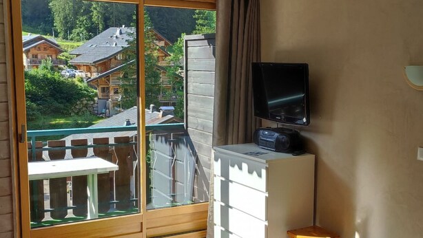 A balcony with a sliding glass door, a television, a small table, and a chair. - Studio 4 Pers, Near Chairlift, South Balcony (Châtel)