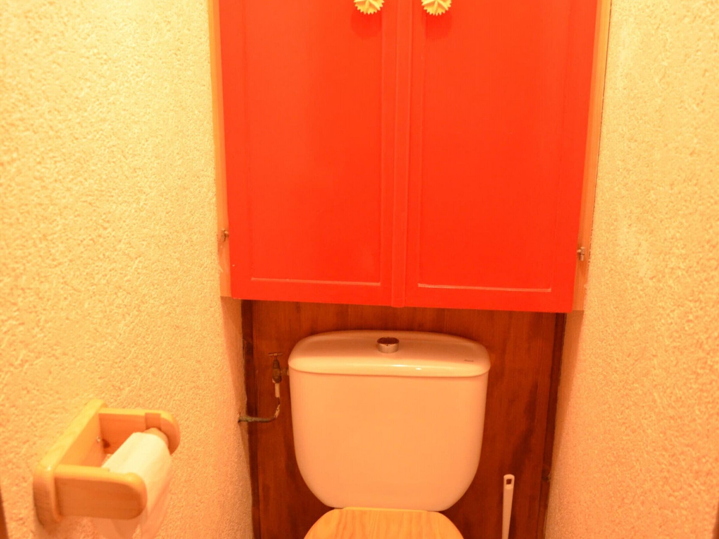 Een badkamer met een houten toilet en een rode kast erboven.