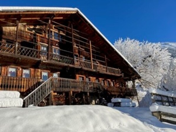 A wooden chalet with a balcony, surrounded by snow-covered trees.