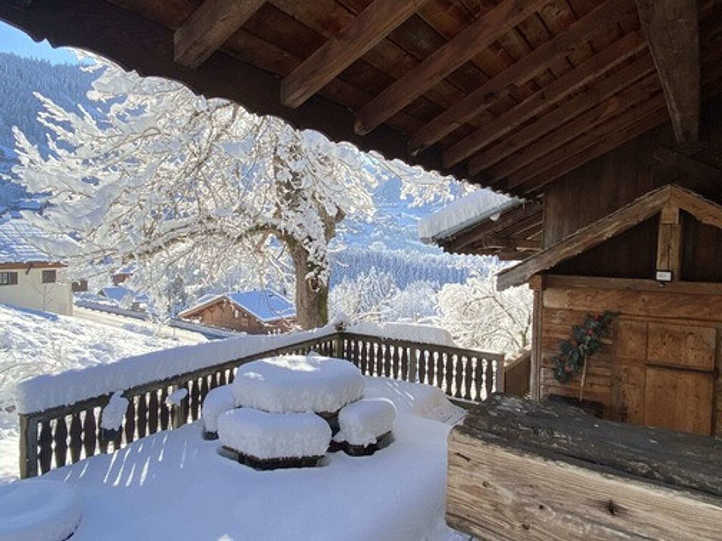 A wooden cabin with a snow-covered deck and a view of a snow-covered mountain.