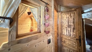 Interior de una cabaña de madera con una ventana, una puerta y una cortina.