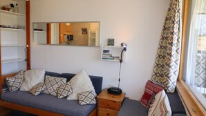 A cozy living room with a sofa, a side table, a mirror, and a window with curtains.