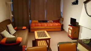 Tunnelmallinen huone, jossa on sohva, pieni pöytä, televisio ja sängyn ympärillä olevat verhot.