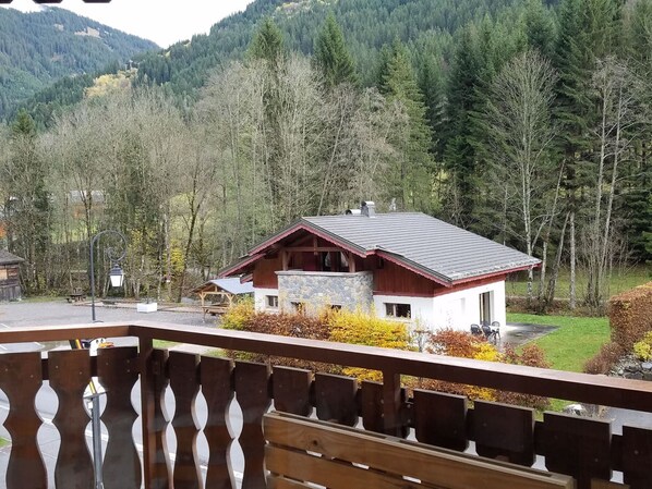 A chalet with a stone foundation, wooden exterior, and a sloped roof, surrounded by forested hills.