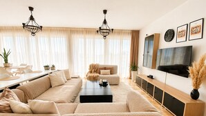 A modern living room with a sectional sofa, a coffee table, a TV, and a dining area with a table and chairs. - Luxury view apartment 10min from Athens airport (Koropi)