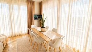 A modern dining area with a long table, white chairs, a potted plant, and a TV on the wall. - Luxury view apartment 10min from Athens airport (Koropi)