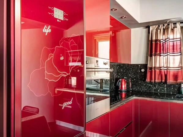 A modern kitchen with red cabinetry, a stainless steel oven, and a red kettle on the countertop.
