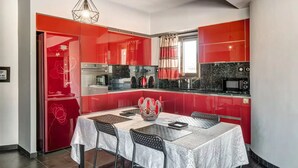 A modern kitchen with red cabinetry, a dining area with a table and chairs, and a hanging light fixture. - Luxury view apartment 10min from Athens airport (Koropi)