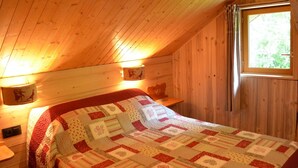 Tunnelmallinen makuuhuone, jossa on puinen katto, tikattu peitto ja kaksi seinälle asennettua lamppua.
