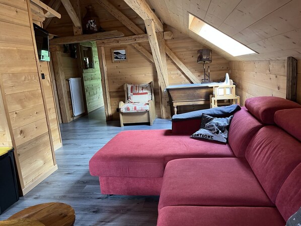 A cozy cabin interior with a red sofa, a wooden chair, and a small table.