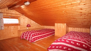 A cozy attic bedroom with wooden walls and sloped ceilings, featuring two beds with patterned bedding and a small table with a lamp. - 3-room apartment for 7 in Châtel, near center and lifts, with balcony and parking (Châtel)