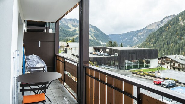 A balcony with a table and chairs, overlooking a mountainous landscape and a parking area. - Cozy 2-Room Apartment for 5 Close to Village & Lifts, Pet-Friendly (Châtel)