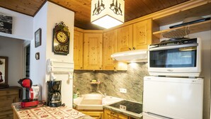 A kitchen with wooden cabinets, a clock, a coffee maker, a microwave, and a refrigerator. - Cozy 2-Room Apartment for 5 Close to Village & Lifts, Pet-Friendly (Châtel)