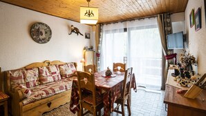 A cozy living room with a wooden ceiling, a wooden sofa with patterned cushions, a dining table with chairs, and a television mounted on the wall. - Cozy 2-Room Apartment for 5 Close to Village & Lifts, Pet-Friendly (Châtel)