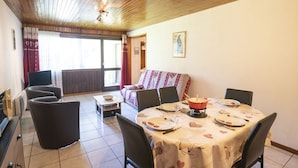 A dining area with a round table set for four, a sofa with a patterned cover, and a view through a glass door to an outdoor area. - Apartment for 5 near cable car, pets allowed (Châtel)