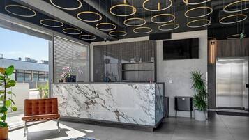 Eine moderne Lobby mit einem Marmor-Empfangstresen, einer Sitzecke mit einem braunen Sessel und einem großen Fernsehbildschirm.