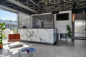 Un vestíbulo moderno con una recepción de mármol, una zona de estar con una silla marrón y una pantalla de televisión grande.