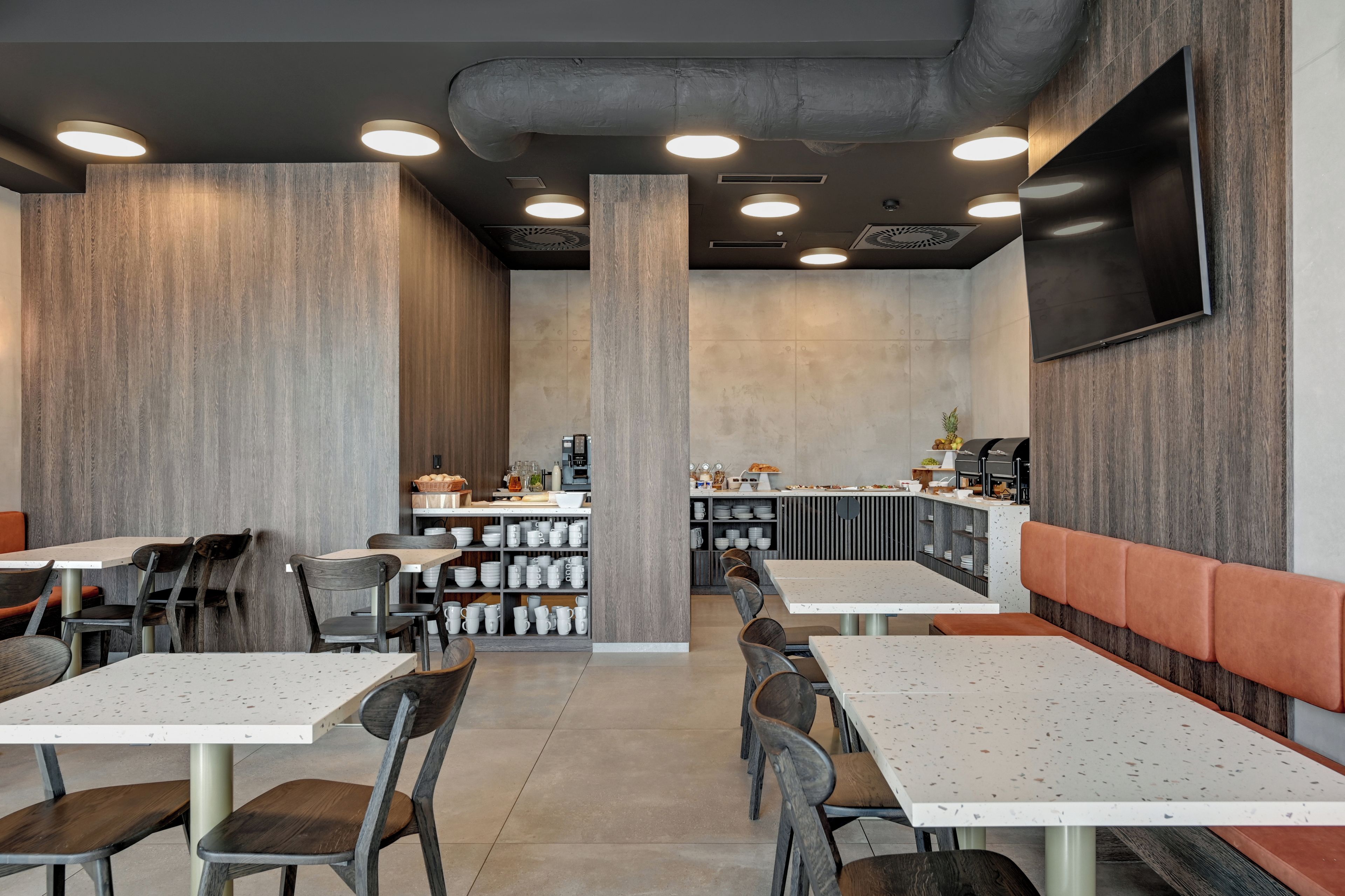 A modern restaurant interior with high tables, chairs, a bar area, and a flat-screen TV mounted on the wall.